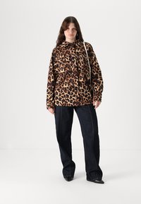 Camicia a stampa leopardata realizzata in morbido tessuto, con design a bottoni e due tasche sul petto, abbinata a jeans blu scuro e scarpe nere.