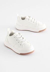 Hvide lædersneakers med rund tå, tekstureret overflade, flade snørebånd og tan gummisål, med ventilationshuller og en bæktrækstrop.