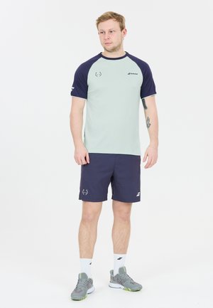 Herretøj til aktiv livsstil bestående af en lysegrøn t-shirt med korte ærmer og marineblå ærmer samt marineblå shorts. Inkluderer grå sportssko og hvide sokker.