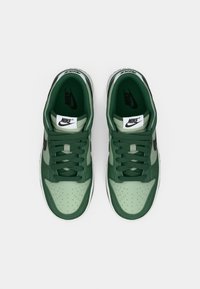 Zöld Nike tornacipő réteges dizájnnal, perforált orr-résszel, fekete swoosh díszítéssel és hozzáillő fűzőkkel. Simább felület a felsőrészén.