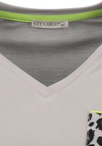 Camiseta de color gris claro con escote en V, que presenta un bolsillo con estampado de leopardo bordeado en verde brillante. Tejido suave con detalles de costura bien acabados.