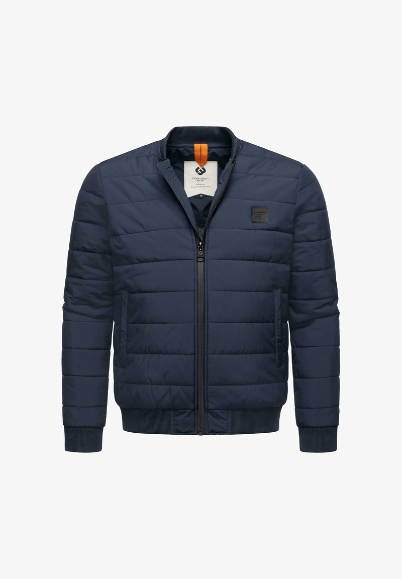 Tamsiai mėlynas siuvinėtas švarkas su priekiniu užtrauktuku, lygiais rankogaliais ir logotipo pleistru ant krūtinės. Yra oranžinės spalvos akcentas ant apykaklės.