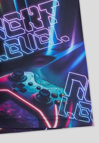 Maglietta grafica con un design di un controller di gioco colorato con accenti luminosi, sfondo blu e viola, e testo in grassetto che recita "PROSSIMO LIVELLO."