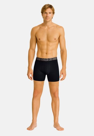 Boxer slip neri con un elastico brandizzato. Il tessuto appare liscio e aderente, offrendo un aspetto slanciato. Il modello è in piedi a piedi nudi.