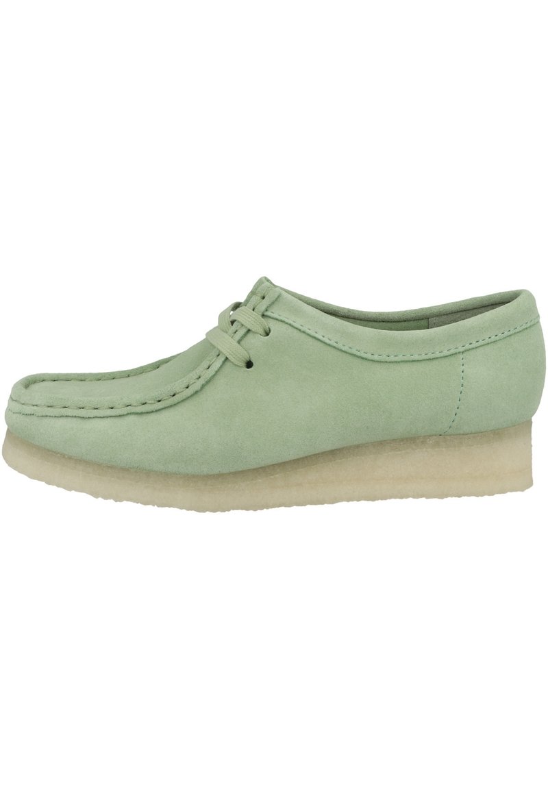 Scarpa in suede verde con una suola a zeppa bassa di colore crema, punta arrotondata e due lacci sottili. Texture liscia con dettagli cuciti.