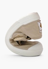 Chaussure enfant en tissu doux beige avec semelle en caoutchouc blanche, pliée pour montrer la flexibilité, avec un petit détail patch au talon.