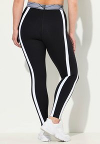 Zwarte leggings met witte zijkanten, hoge tailleband en een gestructureerd grijs paneel. Gecombineerd met witte sportschoenen voor een contrast.