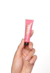 Tube de blush liquide étiqueté "Cheek Heat", avec un corps rose et un capuchon noir ; tenu dans une main, affichant une texture douce et un design léger.