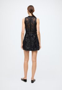 Black sleeveless dress with a sheer embroidered back featuring ornate floral patterns. The skirt is fitted, and the bottom has a smooth texture.