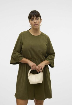 Robe verte jusqu'aux genoux avec des manches bouffantes trois-quarts et une taille froncée, assortie d'un petit sac à main crème. Texture de tissu lisse.