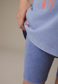 Lysblå bomulds t-shirt med et grafisk design på forsiden, parret med blå ribbede cykeltights. Fokus på tekstur og pasform.