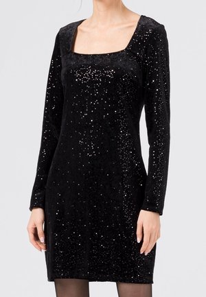 Femme portant une mini robe en velours noir à manches longues, ornée de petits sequins scintillants et dotée d'un décolleté carré.