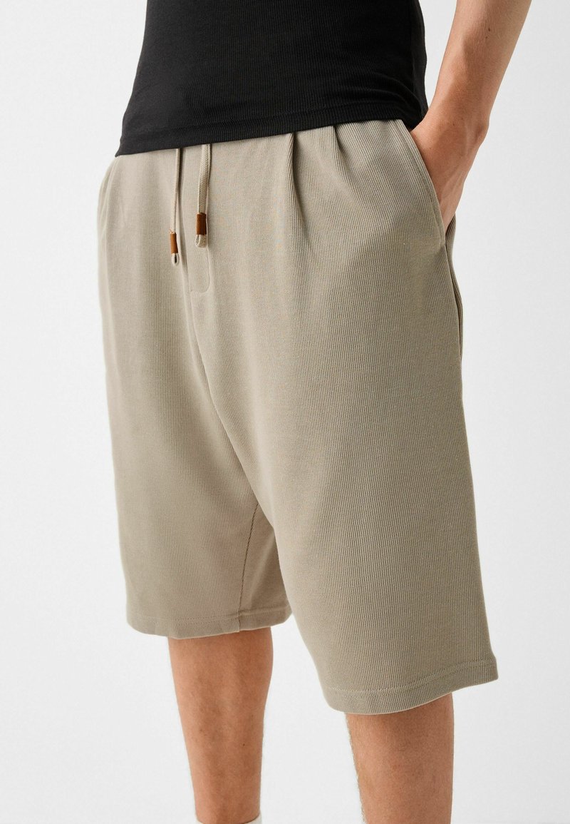 Short beige côtelé avec une ceinture élastique dotée de cordons de serrage et d'accents marron, présenté dans une posture décontractée.