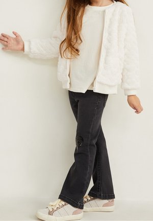 Hvid dunet bomberjakke, cremefarvet top, sorte jeans med palietdetalje på knæet og beige sneakers med pink accenter og sløjfesnørebånd.