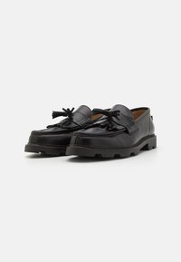 Mustad nahast loafers dekoratiivsete lipsudega, paks kummitald, ääred õmmeldud detailidega, sile tekstuur ja ümar toes.