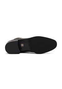 Suela de zapato de cuero negro con agarre texturizado, que presenta una puntera redondeada y un pequeño emblema en la plantilla. Diseño limpio, sin detalles adicionales.
