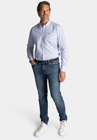 Lichtblauw overhemd met kleine witte stippen, gecombineerd met blauwe jeans en witte sneakers. Voorzien van een borstzak en een bruine riem.