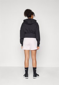 Kratka črna kapuca z ohlapnimi rokavi, v kombinaciji s svetlo roza kratkimi hlačami. Črne športne čevlje in nogavice dopolnjujejo videz.