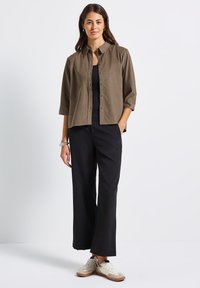 Chemise olive verte à manches retroussées, associée à un pantalon large noir et des baskets légères. Design simple, tissu respirant.