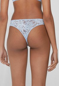 Light blue lace thong with floral pattern, scalloped edges, and minimal back coverage, highlighting intricate texture and detailed design.