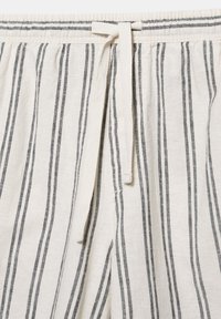 Világos bézs színű lenvászon nadrág függőleges fekete csíkokkal és elöl húzózsinóros derékrésszel, amely állítható illeszkedést biztosít.