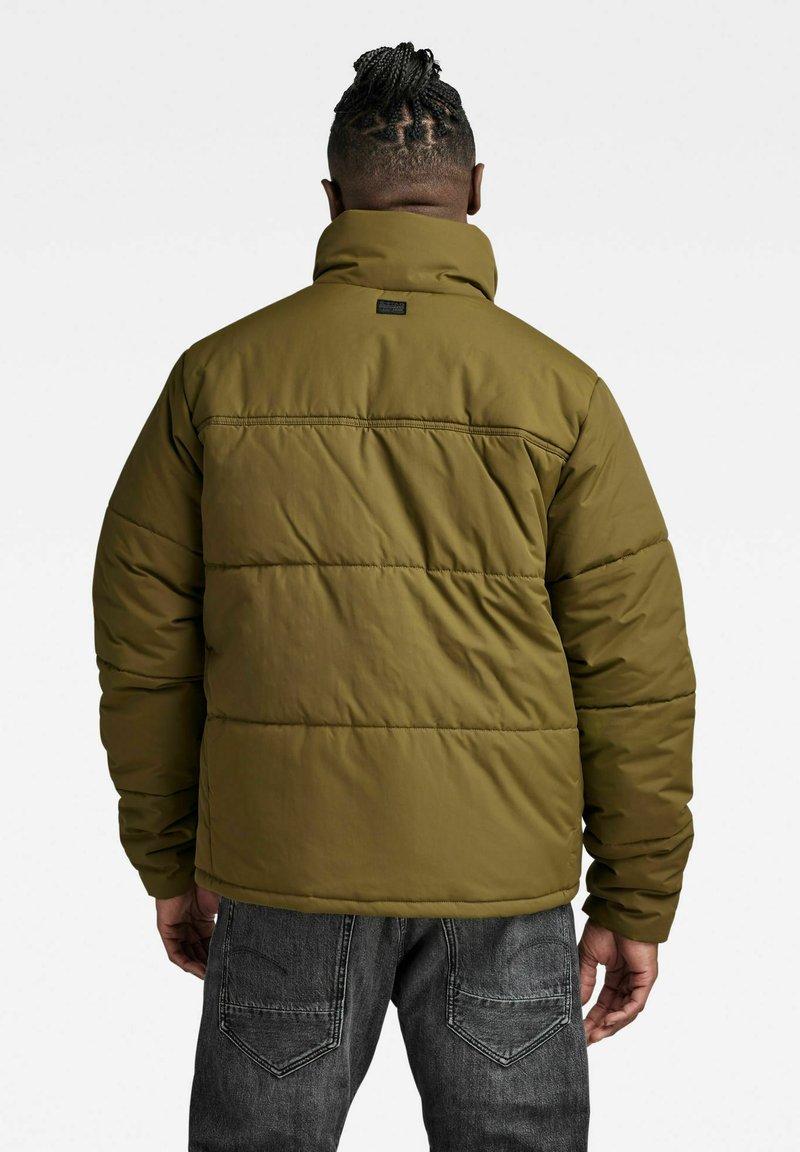 Olijfgroene pufferjack met een hoge kraag, gewatteerde textuur en gestikte details. Bevat een label aan de achterkant en lange mouwen.