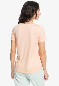Camiseta de color durazno con mangas cortas, textura suave, escote redondeado y un corte relajado. La vista trasera muestra un detalle mínimo.