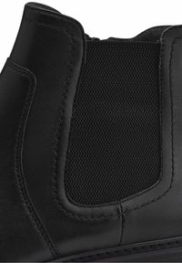 Botte Chelsea en cuir noir en gros plan montrant le panneau latéral élastique, les détails des coutures et la texture lisse.