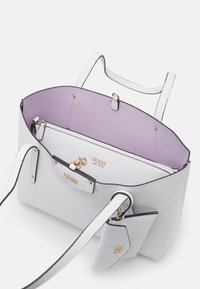 Grå tekstureret håndtaske med kontrasterende lavendel indvendig, med dobbelte håndtag, en lynlåslomme og hardware i guldfarve.