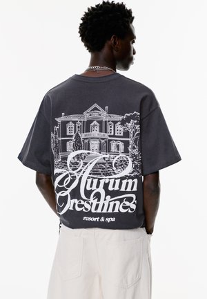 Grå bomulds t-shirt med korte ærmer, med en hvid grafik af et hus og teksten "Aurum Crestlines resort & spa" på ryggen.