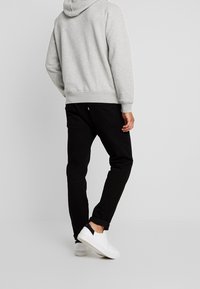 Grau Kapuzenpullover mit Kängurutasche, schwarze Jeans und weiße Sneakers mit marineblauen Akzenten. Einfaches Design, lockere Passform, sichtbares Logo auf den Jeans.