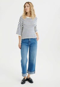 Sweter w paski w kolorze kremowym i granatowym, w połączeniu z dżinsami w kolorze niebieskim z podwiniętymi mankietami i czarnymi loafersami. Sweter ma szerokie rękawy i prążkowaną teksturę.