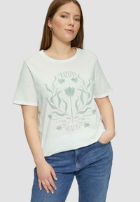 Witte katoenen T-shirt met een groene bloemenafbeelding en de tekst "BLIJ MET DE SCHONE DINGEN". Korte mouwen en een relaxed fit.