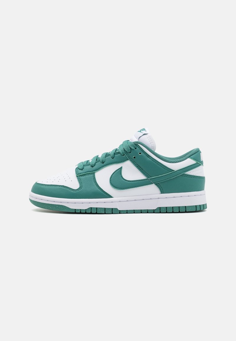Baskets basses Nike blanches et vertes avec lacets, embout perforé et logo Swoosh vert sur le côté, sur un fond uni.
