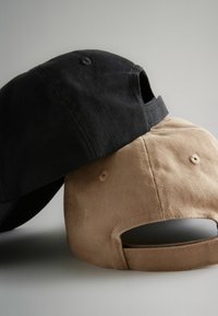 Cappellini da baseball in cotone neri e color t mélange impilati, con finitura texturizzata, visiere curve e cinturini regolabili sul retro.