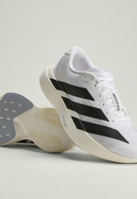 Chaussures de course blanches avec un design à trois bandes noires, une semelle beige épaisse, et un marquage "Adizero" sur la languette et le côté.