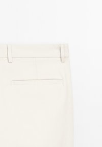 Beige broek met een vlakke tailleband, twee riemlussen en een achterzak. De stof lijkt glad met een nette afwerking, zonder zichtbare patronen.