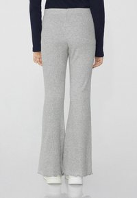 Graue gerippte Schlaghosen mit weicher Textur, hohem Bund und rohen Säumen, kombiniert mit weißen Sneakers. Rückansicht gezeigt.