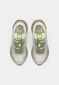 Ζευγάρι λευκά και ανοιχτό γκρι αθλητικά παπούτσια Veja με πράσινες λεπτομέρειες και μπεζ σόλες, σε θέαση από πάνω, σε λευκό φόντο.