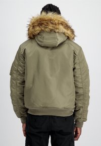 Giacca bomber verde oliva con cappuccio e bordo in pelliccia sintetica, polsini a coste e maniche a contrasto. Presenta tasche con zip e bottoni.