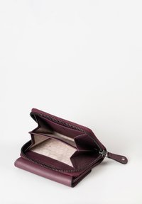 Portafoglio con zip in pelle bordeaux scuro, dotato di due scomparti, foderato con un leggero motivo geometrico. Presenta cuciture e una cerniera metallica.