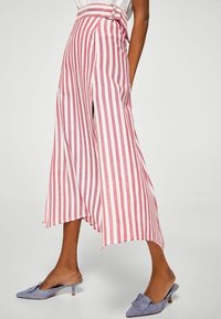 Pantalons larges rayés rouges et blancs avec une taille haute, dotés d'une boucle de ceinture. Tissu doux, ourlet irrégulier et fentes sur les côtés.