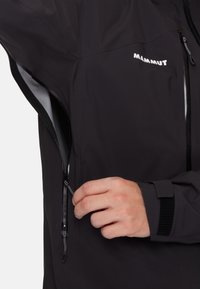 Black waterproof jacket features a zippered pocket, elastic cuff, and textured fabric. Brand logo "Mammut" is visible on the shoulder.