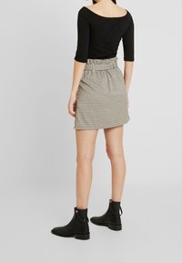 Top nero senza spalle abbinato a una mini gonna a scacchi con vita arricciata e spacco frontale. Indossato con stivali neri alla caviglia.