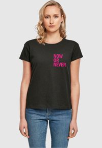 Tricou din bumbac negru, cu mâneci scurte, având textul îndrăzneț de culoare roz "ACUM SAU NICIODATĂ" imprimat vertical pe partea stângă. Design clasic cu guler rotund.