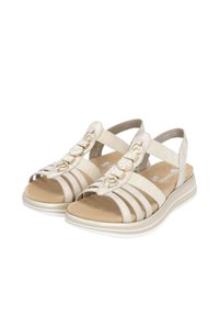 Beige Sandalen mit Stoffriemen und dekorativer Hardware. Weiche Innensohle und gepolsterte, konturierte Außensohle mit weißen und beigen Streifen.