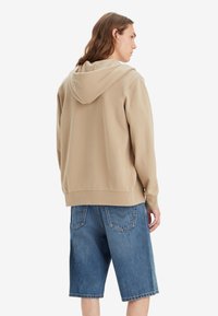 Beige hoodie met een relaxte pasvorm en geribde manchetten, gecombineerd met blauwe denim shorts. Eenvoudig ontwerp, zachte textuur, zonder zichtbare patronen.