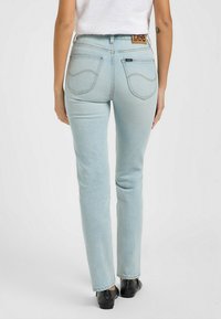Jeans in denim blu chiaro con vestibilità slim, cinque tasche e un'etichetta in pelle marrone con logo sulla cintura posteriore.
