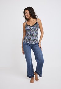 Bloemmotief cami-top met zwarte kanten rand, gecombineerd met wijd-uitlopende spijkerbroek. Beide items hebben levendige kleuren en onderscheidende patronen.