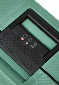 Maleta rígida verde con superficie texturizada, mecanismo de bloqueo negro con tres orificios y un diseño de asa elegante.
